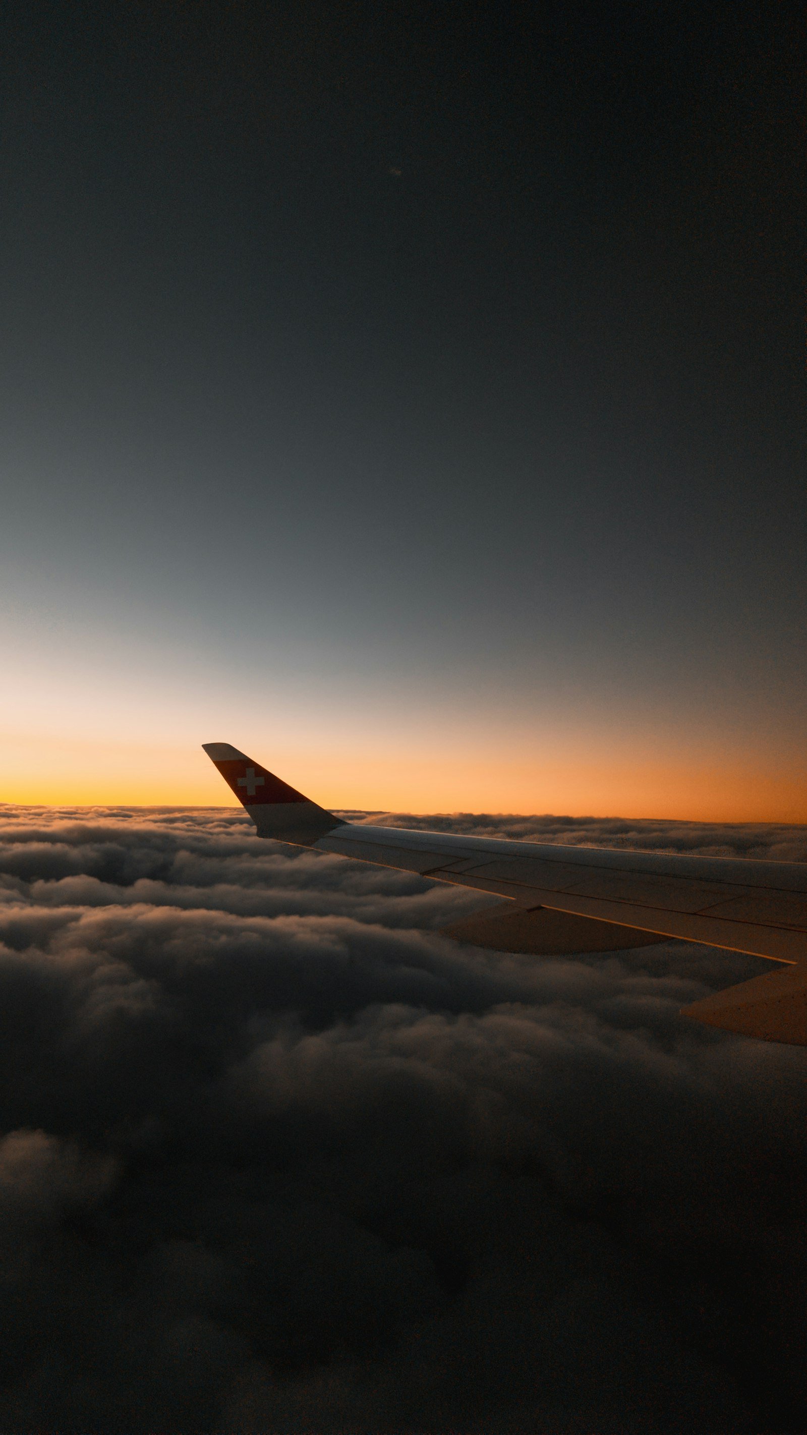 Airplane wing gliding above illuminated clouds at sunset